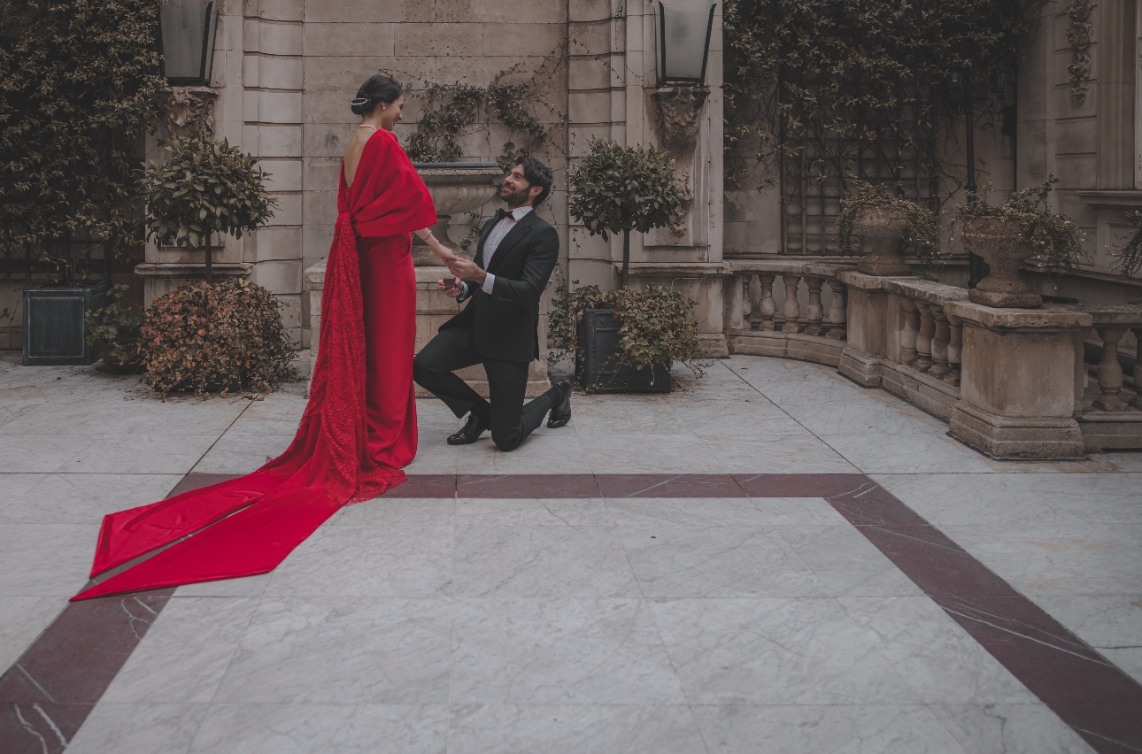 woman in a red dress, man in tux bent down on one knee with ring