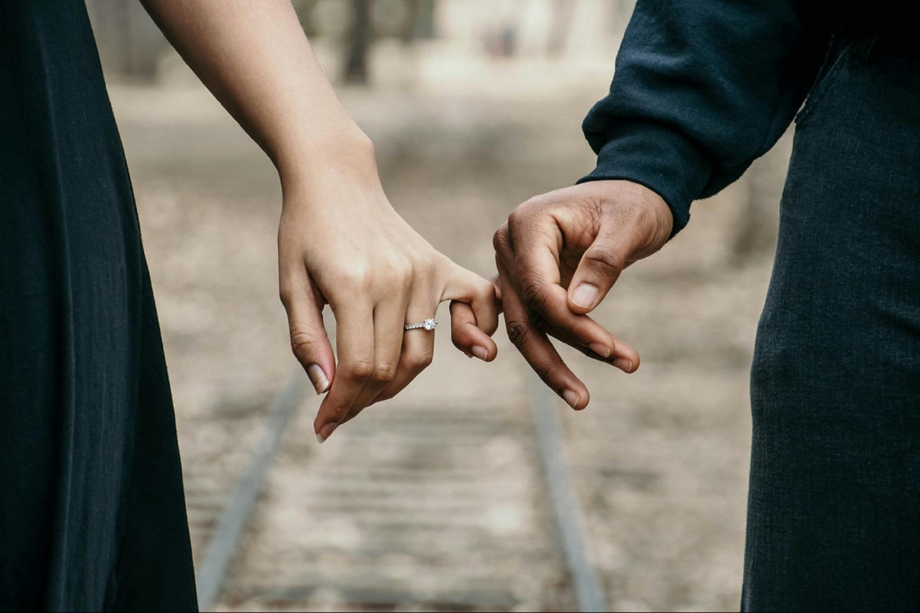 two hands holding by their little finger one wearing an engagement ring