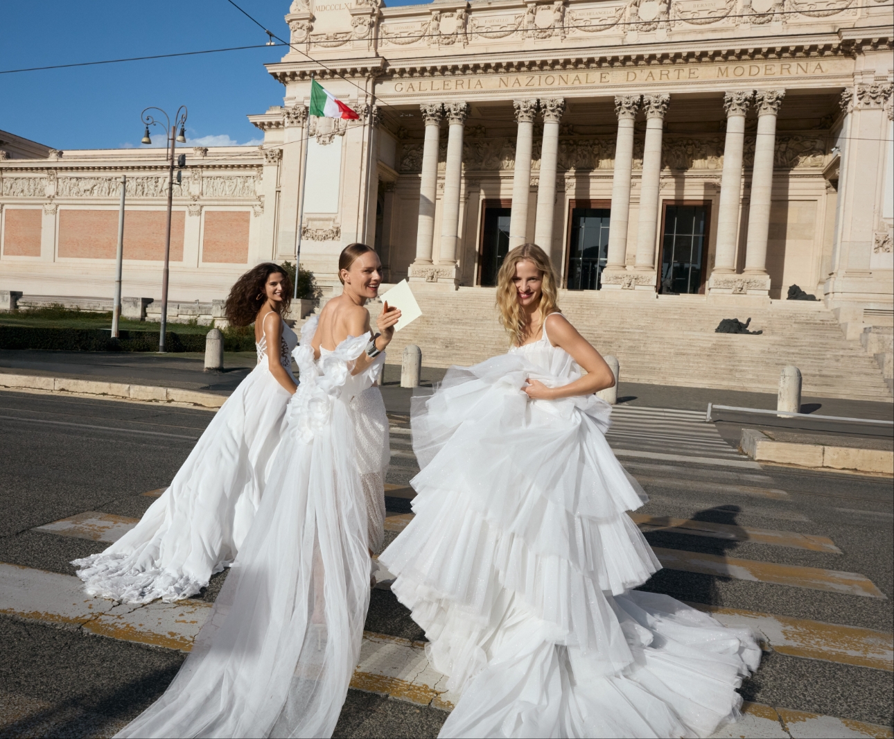 three models in large frilly wedding dresses on the steps of a historic building